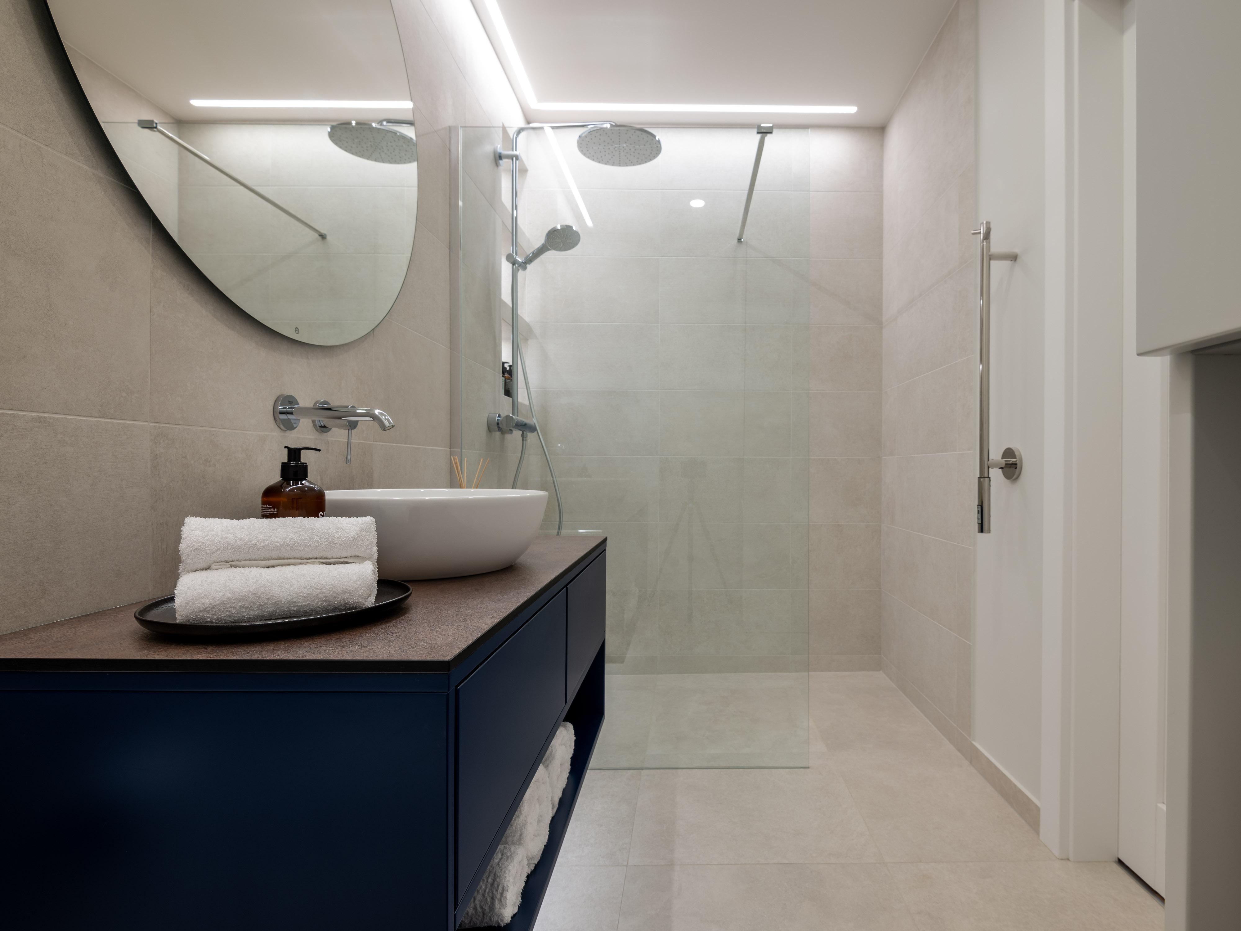 A modern bathroom with a glass shower enclosure, featuring a bathtub to the left, complete with a window and towel. A scoo...